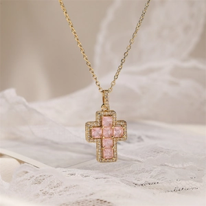 Close-up of gold cross necklace with pink square gemstone and sparkling crystals