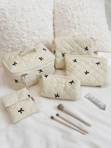 Five-piece beige quilted cosmetic bag set with black bow embroidery on soft plush background