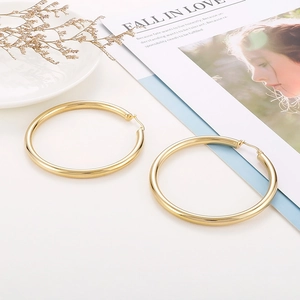 Flat lay of large 18K gold plated titanium steel hoop earrings with magazine and dried flowers