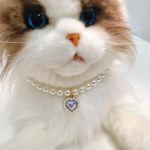 Macro shot of pet pearl necklace with a heart-shaped crystal pendant on a white cat