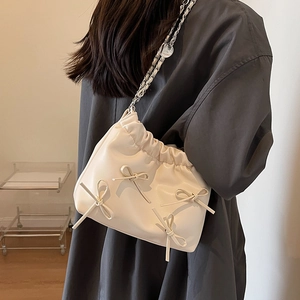 Chic beige leather bucket bag with chain strap and bow detail on a stylish woman