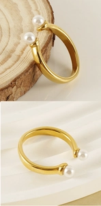 Detailed view of adjustable gold stainless steel ring with dual pearls on wooden base