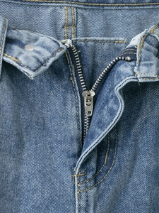 Dettaglio della cerniera in metallo argento e cuciture gialle su jeans in denim blu