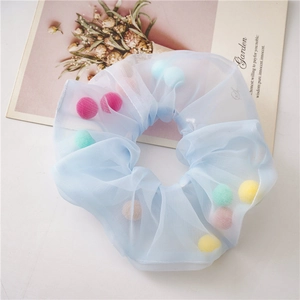 Close-up of blue mesh scrunchie with colorful plush balls inside on white surface