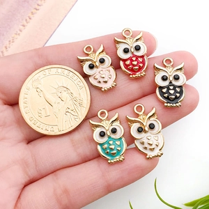 Five colorful owl alloy pendants with enamel coating held for size comparison with a coin