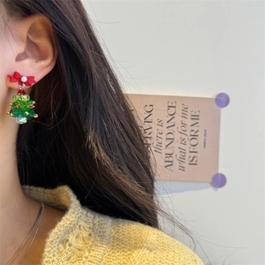 Close-up of beaded Christmas tree earrings with red bow on a model for festive style