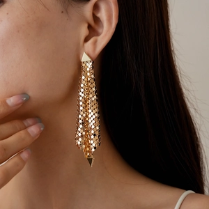 Close-up of golden geometric tassel earrings featuring small metal discs and triangles
