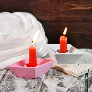 Detailed view of boat-shaped plaster candle holders in pink and white with red candles