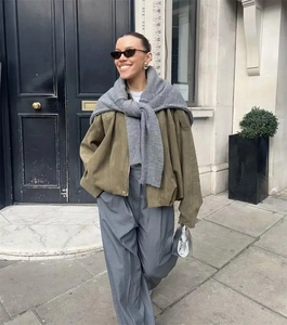 Street style view of a green zip-up bomber jacket with a knitted gray shawl detail