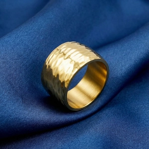 Macro shot of gold stainless steel wide ring with hammered texture on blue silk fabric
