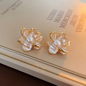 Detailed close-up of golden floral earrings with white petals and pearls on book pages