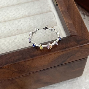 Macro shot of silver open ring with colorful rectangular zircons on dark wood box