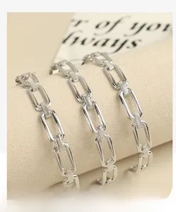 Macro detail of silver geometric chain link bracelets on a minimalist beige pedestal