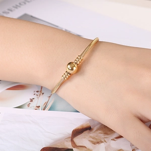 Detailed view of a gold-finish stainless steel cable bracelet with a central polished sphere