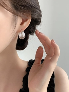 Detail of layered silver C-shape hoop earrings worn on ear showing fine metallic texture