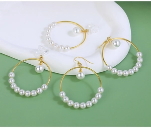 Detailed macro view of large gold hoop earrings set with elegant white pearls on green background