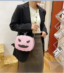 Close-up of pink pumpkin crossbody bag with bat wings and gold chain on a model