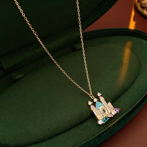 Close-up of gold-plated castle pendant with blue and purple gems in green velvet box