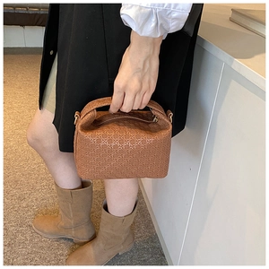 Close-up of brown woven texture PU leather pillow bag held by model in indoor setting