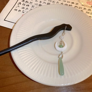 Detailed view of a Chinese wooden hairpin with moon and jade-like pendants on ceramic plate