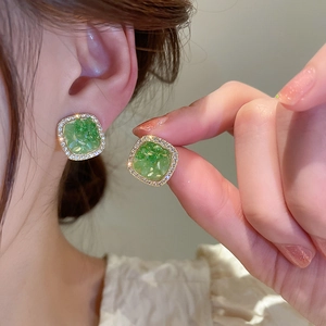 Close-up of square green resin earring with golden frame and sparkling rhinestones