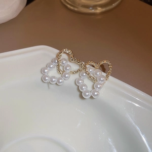 Elegant gold hammered metal and white pearl double heart earrings on a ceramic dish