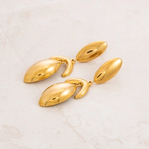 Macro view of gold-plated stainless steel oval earrings on a light marble background