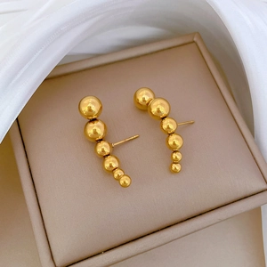 Close-up of golden beaded curved stud earrings placed on a premium beige jewelry box