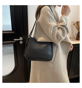 Detail shot of a black PU leather crescent shoulder bag worn by a model in a stylish interior