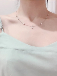 Detail of silver clover necklace with floral charms worn on woman's collarbone
