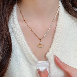 Detail of maple leaf pendant with pearl and asymmetrical gold chain on white sweater