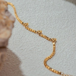 Macro view of gold heart charms on a delicate square link stainless steel bracelet
