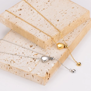 Minimalist tassel heart necklace set in gold and silver finish on textured stone pedestal