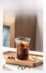 Close-up of ribbed glass cup with dark walnut wood heat-insulating sleeve on wooden tray