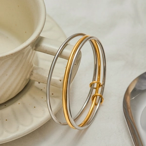 Polished stainless steel stackable bangles in gold and silver on a ceramic cup handle
