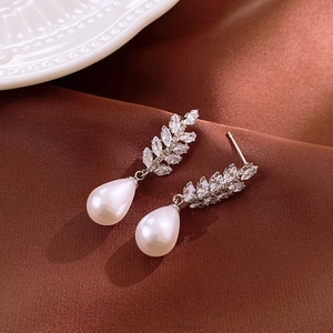Elegant wheat-shaped zircon earrings with white drop pearls on dark brown satin background