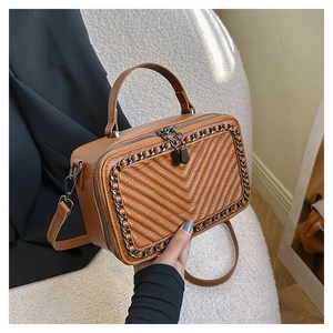 Dettaglio di una borsa marrone trapuntata con catena in metallo e manico in un set lifestyle
