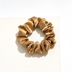 Close-up of golden satin scrunchie showing smooth silk texture and pleated design details