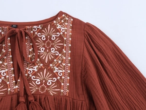 Close-up of intricate embroidery and textured fabric on a reddish-brown mini dress