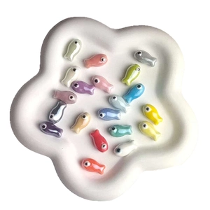 Colorful fish-shaped ceramic beads for DIY jewelry displayed on a white petal tray