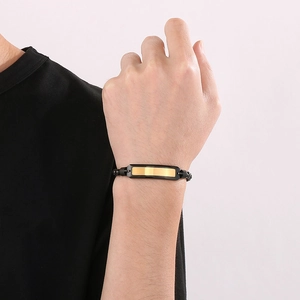 Detail of a minimalist gold plate bracelet with black silicone strap on a male wrist