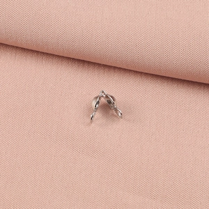 Macro view of a single silver metal crimp bead cover for DIY jewelry crafting on pink fabric