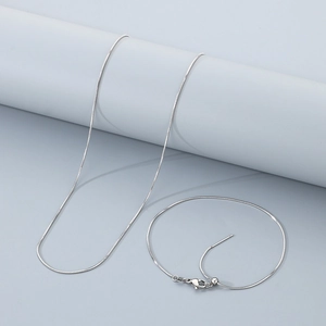 Silver snake chain jewelry set with adjustable sliding clasp on light gray background