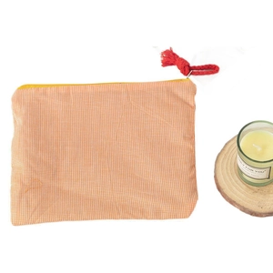 Minimalistische orangefarbene Tasche mit Karomuster und roter Quaste auf weißem Hintergrund