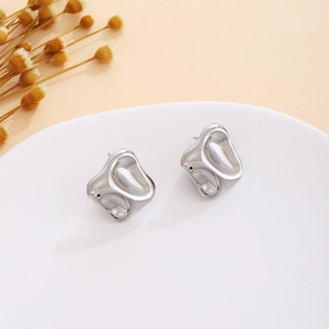 Detail view of silver textured earrings with liquid metal geometric wave design on white stand