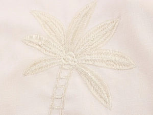 Close-up of palm tree embroidery detail on beige linen textured summer vacation shirt