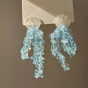 Macro detail of long beaded tassel earrings with light blue stones on a white card