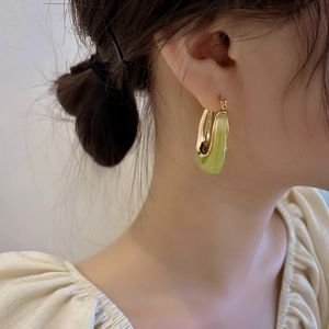 Detail of elegant U-shaped gold earrings with translucent green resin on model ear