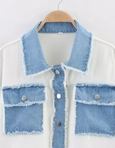 Detail of white and blue patchwork denim jacket with frayed edges and metal buttons
