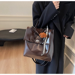 Detail of dark brown leather tote bag with a cute teddy bear pendant and glossy finish